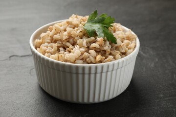 Tasty pearl barley porridge in bowl on dark textured table, closeup