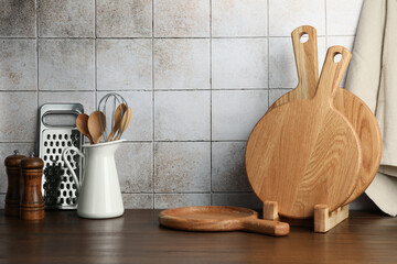 Wooden cutting boards and kitchen utensils on table near tiled wall