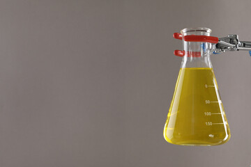 Retort stand and laboratory flask with liquid on light grey background, closeup. Space for text