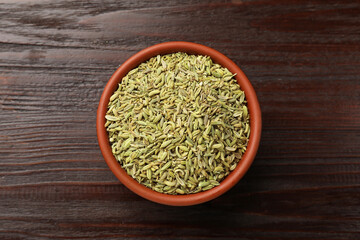 Fennel seeds in bowl on wooden table, top view