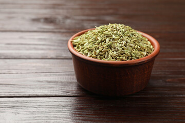 Fennel seeds in bowl on wooden table, closeup. Space for text
