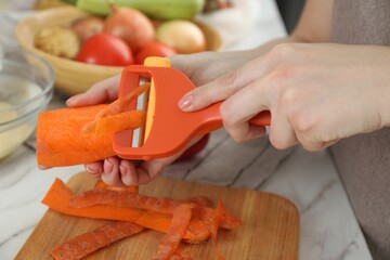 Woman peeling fresh carrot at white marble table, closeup