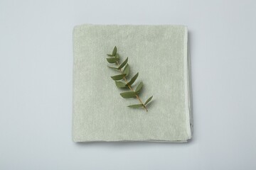 Soft green towel and eucalyptus branch on light grey background, top view
