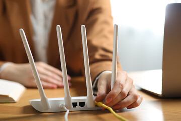 Woman connecting cable to Wi-Fi router at table indoors, closeup