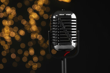 Vintage microphone against black background with blurred lights, closeup. Sound recording and reinforcement