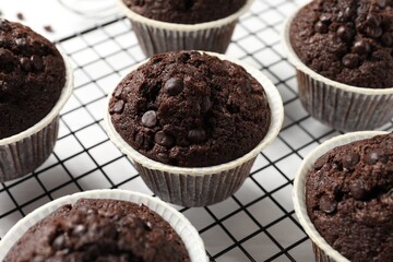 Tasty chocolate muffins and cooling rack on white table, closeup