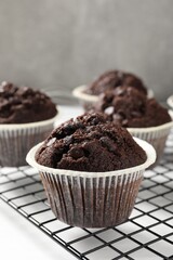 Tasty chocolate muffins and cooling rack on white table, closeup