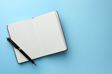 Open notebook with blank pages and pen on light blue background, top view. Space for text - obrazy, fototapety, plakaty