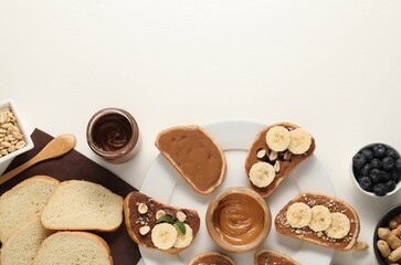 Toasts with different nut butters, banana slices, blueberries and nuts on white table, flat lay....