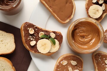 Toasts with different nut butters, banana slices, blueberries and nuts on white table, flat lay