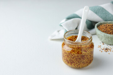 Whole grain mustard and spoon in jar on white table. Space for text