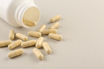 Bottle and vitamin capsules on light background, closeup. Space for text