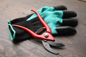 Pair of claw gardening gloves and secateurs on wooden table, closeup