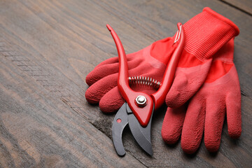 Pair of red gardening gloves and secateurs on wooden table, space for text