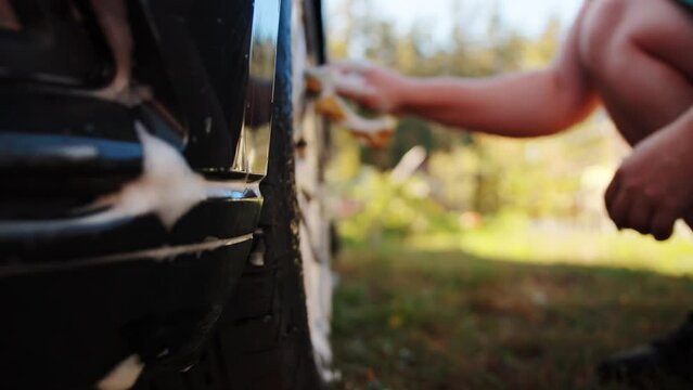 Hand washing car wheel rims with a sponge and shampoo in nature. Slow motion