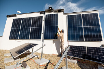 Man installing solar panels on vertical wall on a rooftop of his house for self consumption....
