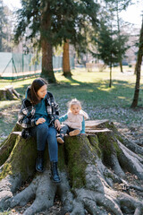 Mom with a little girl sits on a huge stump in a coniferous forest