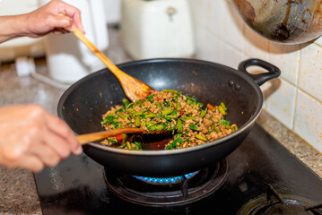 Woman cooking stir-fried pork with basil in real life home kitchen, Thai style food. Selective focus image.