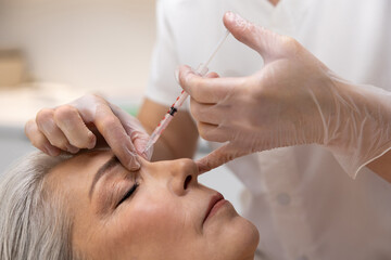 Beautician injecting filler into forehead of a female patient
