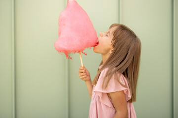 Portrait of a little girl with pink cotton candy on green wall background outdoors. Happy kids...