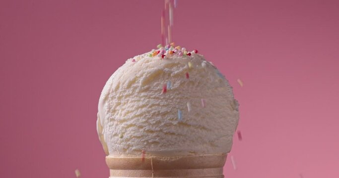 close-up of decorative sugar sprinkles falling on an ice cream ball on a pink background