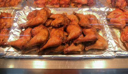 Roasted marinated chicken thighs for sale on display in thermal counter in deli department of supermarket