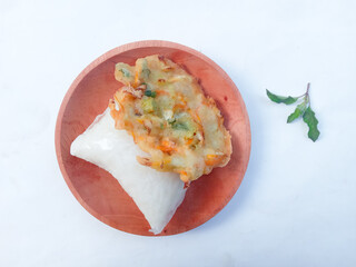 bakwan and lontong on a wooden plate on a white background. Bakwan is sliced ​​cabbage and carrots mixed with flour and then fried. lontong is rice put in plastic or banana leaves and then boiled.