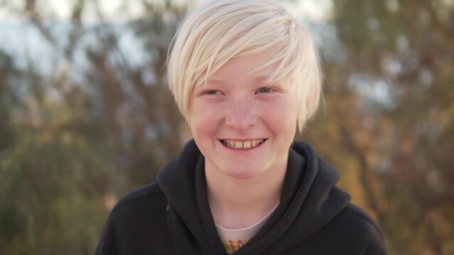 Close-up of blond boy with thick white hair on nature park background,