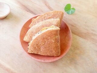 pieces of martabak filled with chocolate sprinkles on a wooden plate on a wooden background....