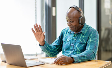 Portrait of happy African American senior man 60 years old  wearing headphones, enjoying working at...