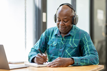 Portrait of happy African American senior man 60 years old  wearing headphones, enjoying working at...