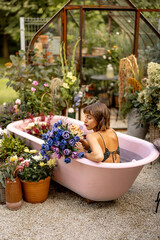 Woman lying in pink bathtub with lots of flowers in garden outdoors. Concept of beauty, bizarre and...
