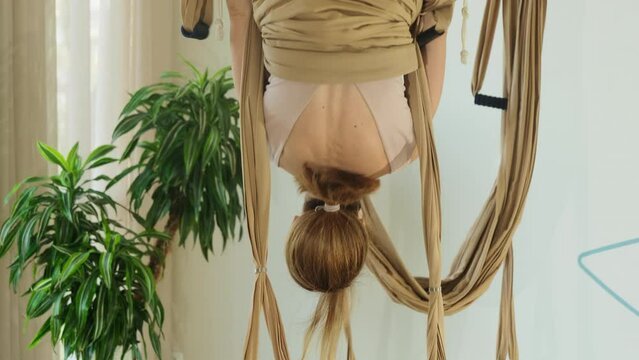 Woman does balance exercises using textile hammock in aero yoga studio. Athletic lady does twirl focusing on aerial technique. Yoga workout
