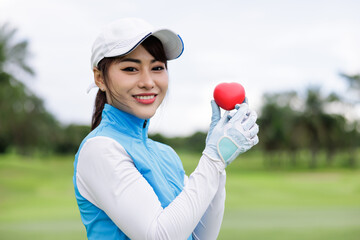 Portrait head shot of young asian female golfer holding red heart at the course over white sky background,