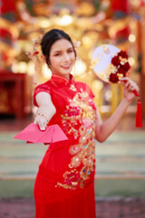 Portrait of young asian woman with traditional Chinese red drese, standing smilling holding angpao envelope inside the temple, Chinese new year , concept