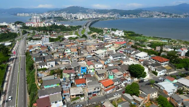 Aerial shot drone orbits to right over favela on hill with two bridges going to Florianópolis in background