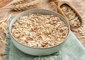 Bowl of dry oats and wheat flakes on wooden table. Top view.