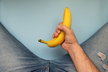 yellow big banana and men's legs in jeans on a blue background. The concept of men's health