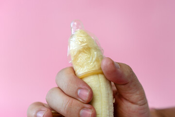Hand shows how to put a condom on the penis using a banana as demonstration. concept of protection against sexually transmitted diseases