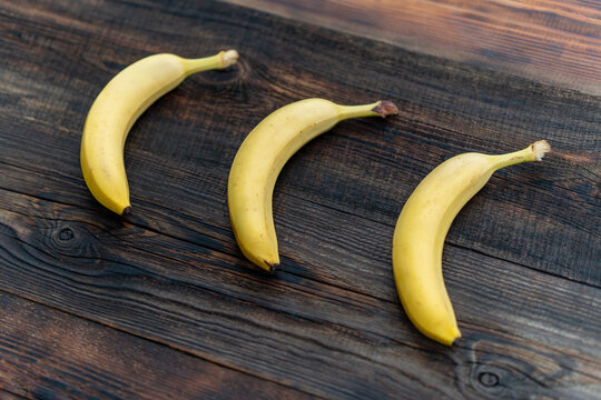 Three bananas lie on a wooden table, tasty and fragrant fruits