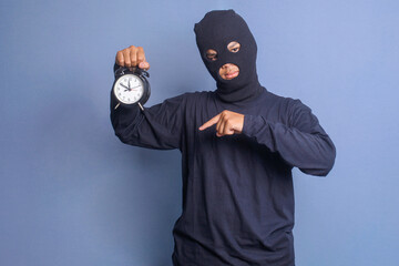 Angry man in black mask pointing with finger at alarm clock