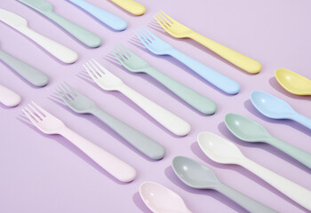 Colorful plastic knives, forks and spoons on a purple background. Birthday party celebration table.