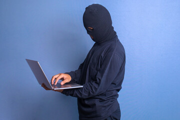 Thief hacker stealing data from laptop computer isolated over blue studio background
