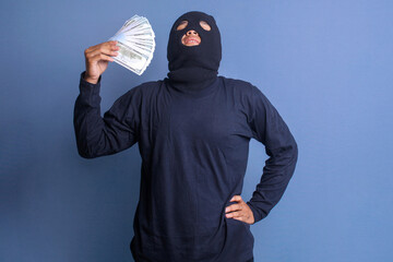 Male thief with balaclava holding a handful of dollar bills with happy gesture
