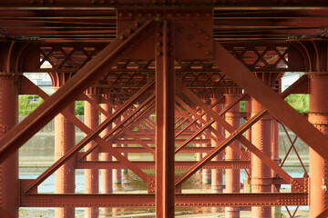川にかかる赤い鉄橋と橋脚が生み出す幾何学模様	