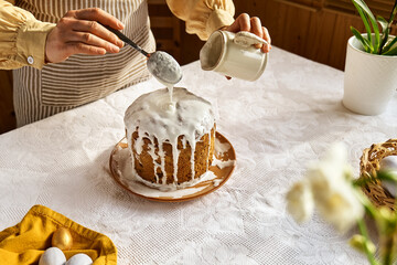 Female hands pouring icing on Easter cake. Traditional easter cake or sweet bread with topping....