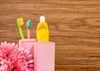 A bright yellow tube of toothpaste in a pink toothbrush container. Colorful toothbrushes and fresh...