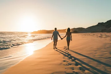  A young couple walking hand in hand along a sandy beach at sunset, leaving footprints in their wake. © apratim
