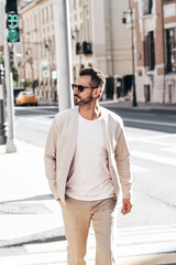 Fototapeta premium Handsome confident stylish hipster lambersexual model. Sexy modern man dressed in elegant white suit jacket. Fashion male posing in the street background in Europe city at sunset. In sunglasses