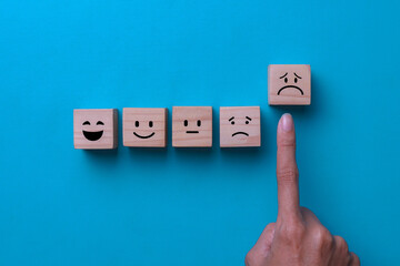 Customer service evaluation and satisfaction survey concepts. Sad face icon on wooden cube on blue...
